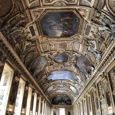 A long gallery under a coffered, painted ceiling, pictures lining the walls