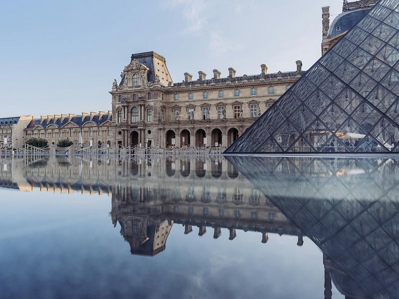 The palace facade and the glass pyramid mirrored in the courtyard fountain basin