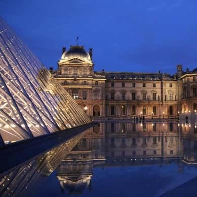 The lit glass pyramid and the palace wing against a deep blue evening sky