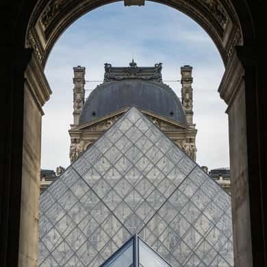 The glass pyramid seen through a stone archway of the palace