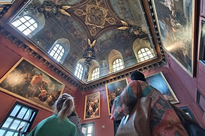 Visitors looking up at a painted, gilded ceiling in a red-walled picture gallery