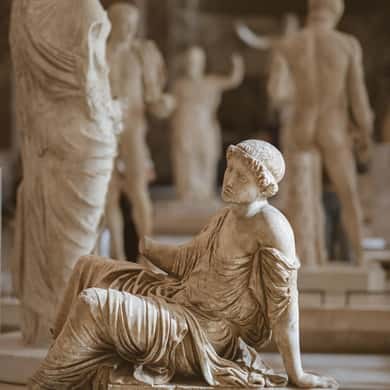 A reclining marble figure in front of a row of ancient statues
