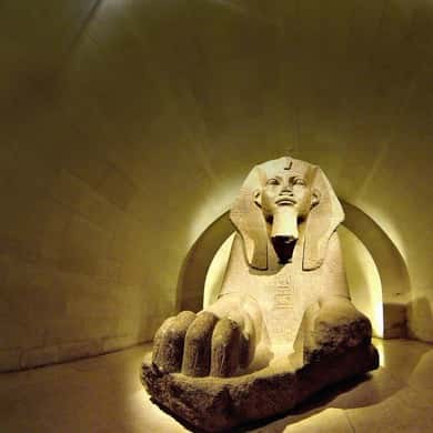 A sphinx lit warm against a dark stone wall